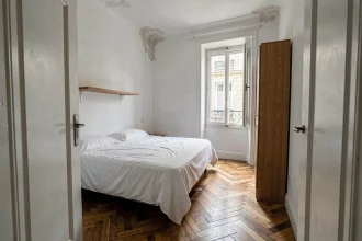 Petite chambre de moins de 9m² dans un appartement Airbnb parisien, avec parquet en chevrons et fenêtre donnant sur cour
